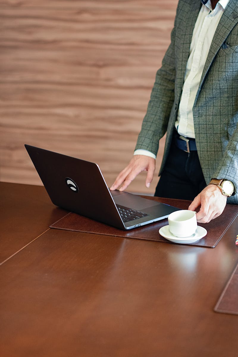 Business professional in a suit using a laptop on a wooden desk with a cup of coffee.